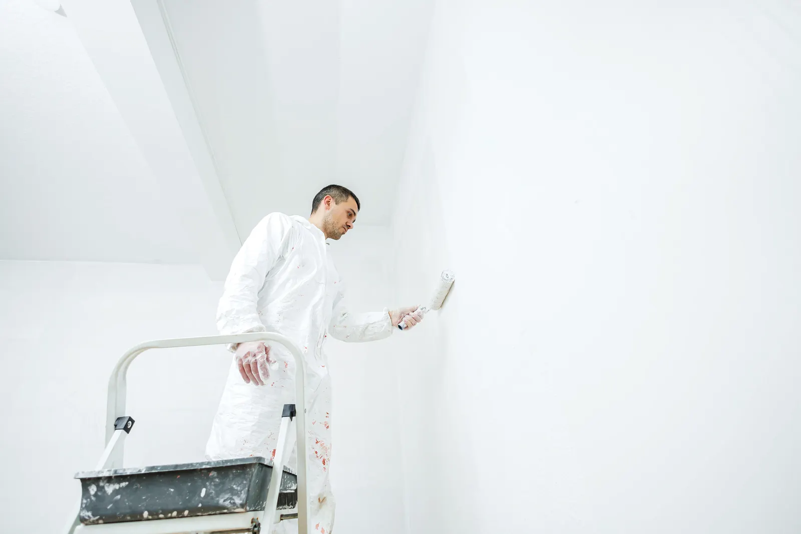 Pintor con rodillo de mango corto en una pared blanca